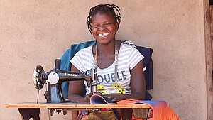 Stärkung von Mädchen durch berufliche Bildung in Malawi Junge Frau lächelt an einer Nähmaschine, während sie bunte Stoffe verarbeitet