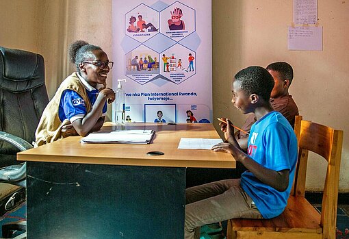 Eine Frau sitzt an einem Schreibtisch und spricht mit zwei Jungen