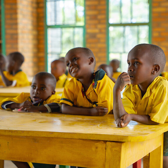 Kinder sitzen an Schultischen und sehen neugierig zur Tafel