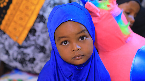 Ein Mädchen aus Äthiopien guckt neutral in die Kamera, hinter ihr sind Spielsachen aus einem child friendly space zu sehen.