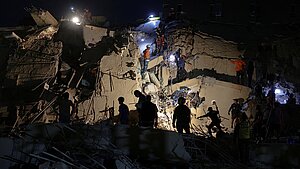 Nachtaufnahme eines eingestürzten Gebäudes, das beleuchtet wird und auf dem sich Rettungskräfte befinden
