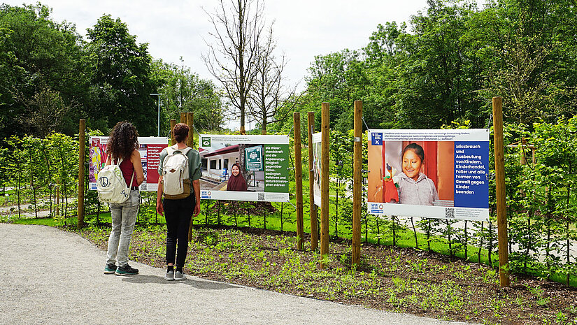 3 sichtbare Plakate mit Bildern und Texten zu den Zielen für nachhaltige Entwicklung (SDGs) 8, 13 und 16, aufgestellt im Park bei der Landesgartenschau in Wangen 2024.