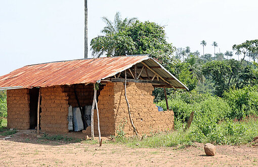 Blick auf ein halb verfallenes kleines Gebäude aus Lehmziegeln und mit rostigem Wellblechdach