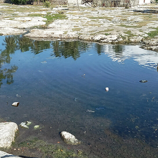 Ein Tümpel, an dem ein Mädchen sitzt und Wasser schöpft