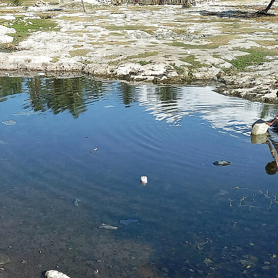 Ein Tümpel, an dem ein Mädchen sitzt und Wasser schöpft