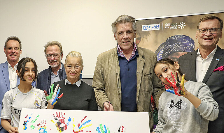 Mehrere Personen, darunter Kinder, stehen vor einem bunt gestalteten Plakat