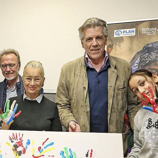 Mehrere Personen, darunter Kinder, stehen vor einem bunt gestalteten Plakat