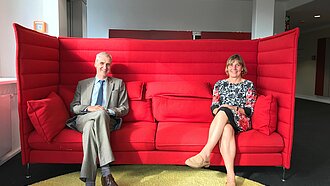 Gemeinsam auf dem roten Sofa - mit der aktuell nötigen Distanz: Dr. Arne Nilsson und Maike Röttger. ©Plan International