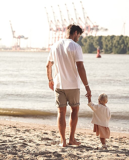 Influencer Jan Möller mit seiner kleinen Tochter am Elbstrand in Hamburg Ein Mann hält ein kleines Mädchen an der Hand und läuft über einen Strand