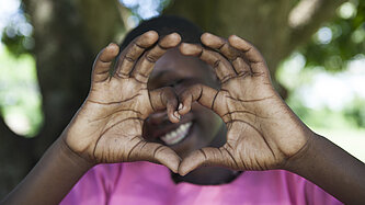 Ein Mädchen aus Uganda zeigt mit ihren Händen ein Herz, um Dankbarkeit und Liebe auszudrücken.