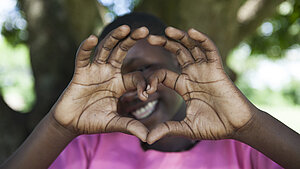 Ein Mädchen aus Uganda zeigt mit ihren Händen ein Herz, um Dankbarkeit und Liebe auszudrücken.