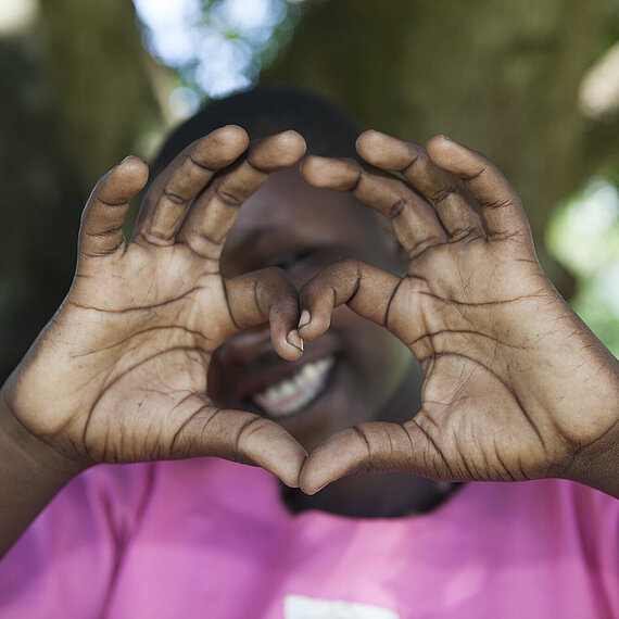 Mädchen zeigt mit Händen ein Herz, symbolisiert Dankbarkeit und Liebe. Ein Mädchen aus Uganda zeigt mit ihren Händen ein Herz, um Dankbarkeit und Liebe auszudrücken.
