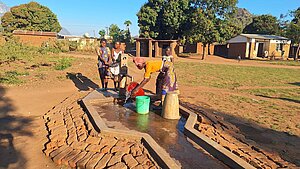 Frau und Kinder holen Wasser aus einem Brunnen in Malawi