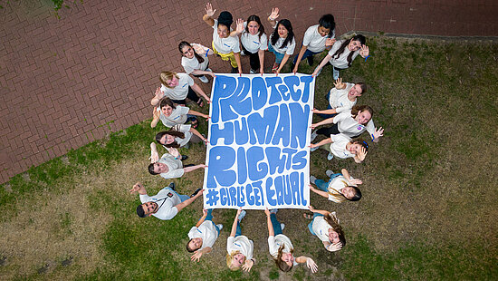Eine Gruppe von Jugendlichen hält ein Plakat mit der Aufschrift "Protect Human Rights #GirlsGetEqual" in die Kamera