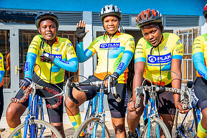 Drei junge Frauen posieren mit Helmen und Sportbekleidung auf ihren Fahrrädern