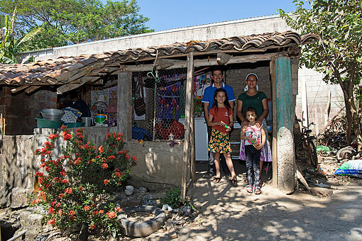 Eine Familie mit zwei jungen Mädchen steht vor einer kleinen Hütte