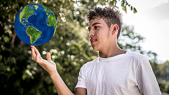 ein Junge balanciert eine Weltkugel auf dem Zeigefinger