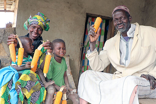 Ein Paar und ein Kind halten getrocknete Maiskolben lächelnd in die Kamera