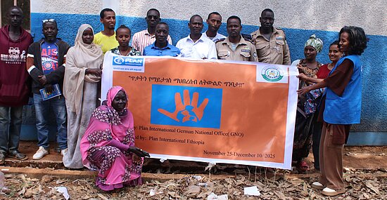 Eine Gruppe von Menschen posiert im Freien mit einem großen, orange-blauen Banner mit dem Logo von Plan International.