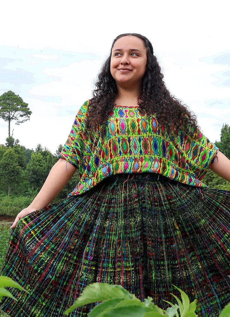 Jaqueline steht in der Mitte einer grünen Wiese und blickt selbstbewusst in die Kamera.