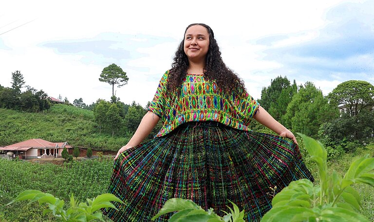 Jaqueline steht in der Mitte einer grünen Wiese und blickt selbstbewusst in die Kamera.