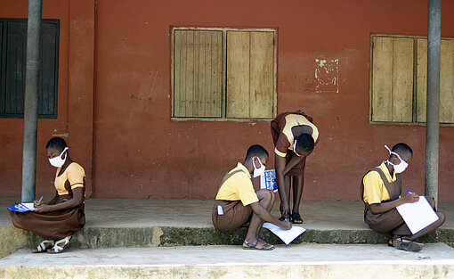 Vier Mädchen sitzen vor dem Schulgebäude und erledigen Aufgaben.
