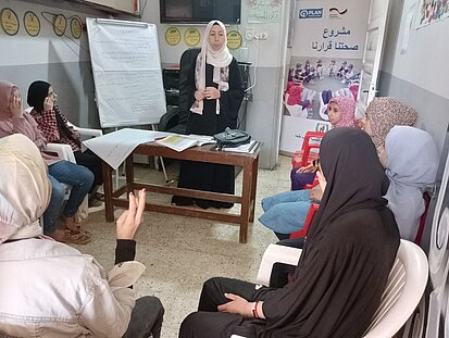 Eine Frau steht vor einem Flipchart, andere Frauen melden sich