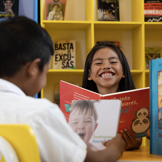 Ein Mädchen hält ein aufgeschlagenes Buch und grinst
