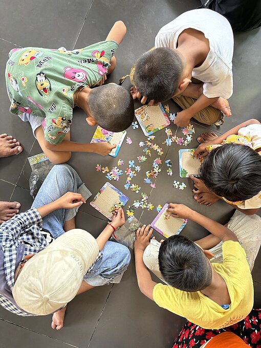 Ansicht aus der Vogelperspektive auf fünf Kinder, die auf dem Boden puzzlen