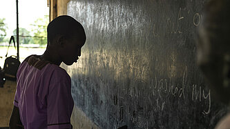 Ein Mädchen in Schuluniform schreibt im Klassenraum an die Tafel. 