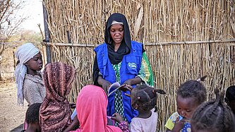 Eine Frau mit Plan-Logo an der Jacke spricht mit Kindrern