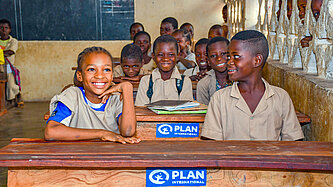 Lachende Schulkinder in einem Klassenzimmer in Benin, unterstützt von Plan International