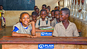 Lachende Schulkinder in einem Klassenzimmer in Benin, unterstützt von Plan International