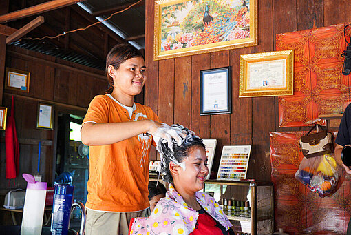 Eine Frau steht hinter einer anderen Frau und shampooniert dieser die Haare