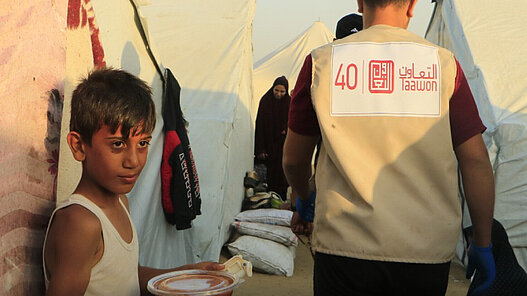 Ein Kind im Gazastreifen erhält warme Mahlzeit von Plan-Partner Taawon. © Taawon Welfare Association