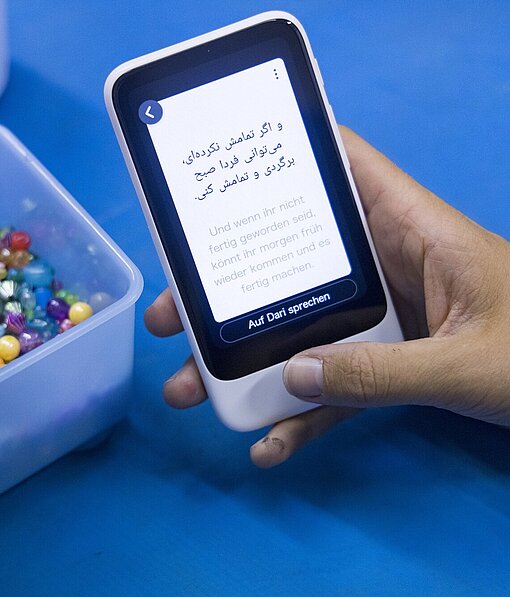 Eine Hand hält einen Digitalen Dolmetscher, auf dem ein Text in zwei Sprachen steht