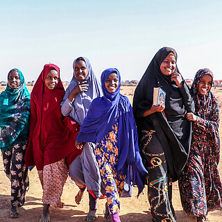 Eine Gruppe von Mädchen läuft durch eine trockene Landschaft, sie lächeln