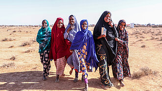 Eine Gruppe Mädchen läuft durch eine trockene Landschaft, sie lachen.