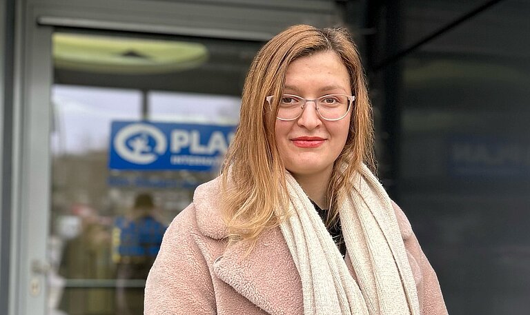 Oksana steht vor dem Pan-Gebäude und schaut in die Kamera