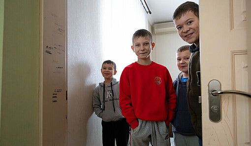 Vier Kinder der Pflegefamilie stehen lächelnd im Haus