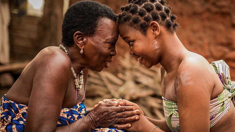 Eine junge und eine ältere Frau, Stirn an Stirn, halten sich an den Händen