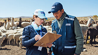 Eine Frau und ein Mann mit dem Logo vomn Plan International auf ihrer Bekleidung beraten sich über eine Liste gebeugt