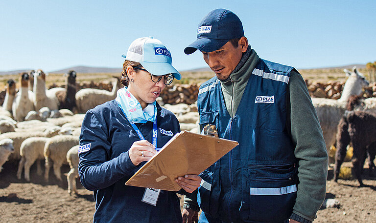 Eine Frau und ein Mann mit dem Logo von Plan International auf ihrer Bekleidung beraten sich über eine Liste gebeugt