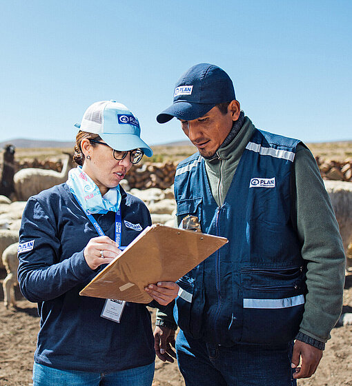 Eine Frau und ein Mann mit dem Logo von Plan International auf ihrer Bekleidung beraten sich über eine Liste gebeugt