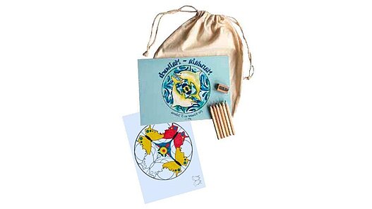 Das Malbuch mit einem halb ausgemalten Blatt. stifte, Anspitzer liegen darauf, der helle Baumwollbeutel darunter.