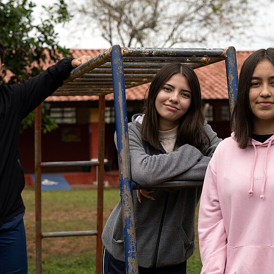 Drei Jugendliche posieren an einem Klettergerüst auf einem Spielplatz