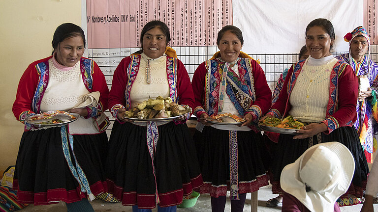 Vier Frauen präsentieren große Teller mit Essen.