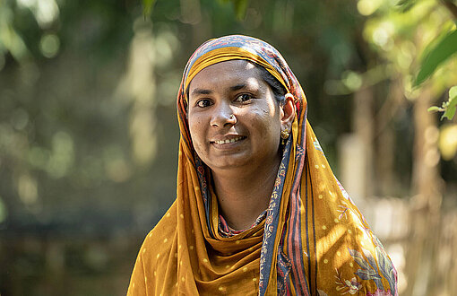 Eine Frau mit einem Kopftuch stecht unter Bäumen
