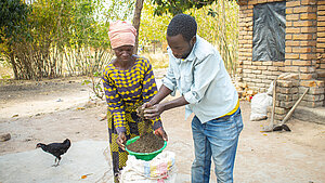 Zwei Personen mischen organischen Dünger auf einem Hof in Malawi