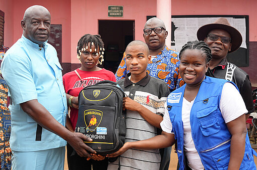 Sechs Menschen stehen als Gruppe zusammen, einem wird ein Rucksack überreicht
